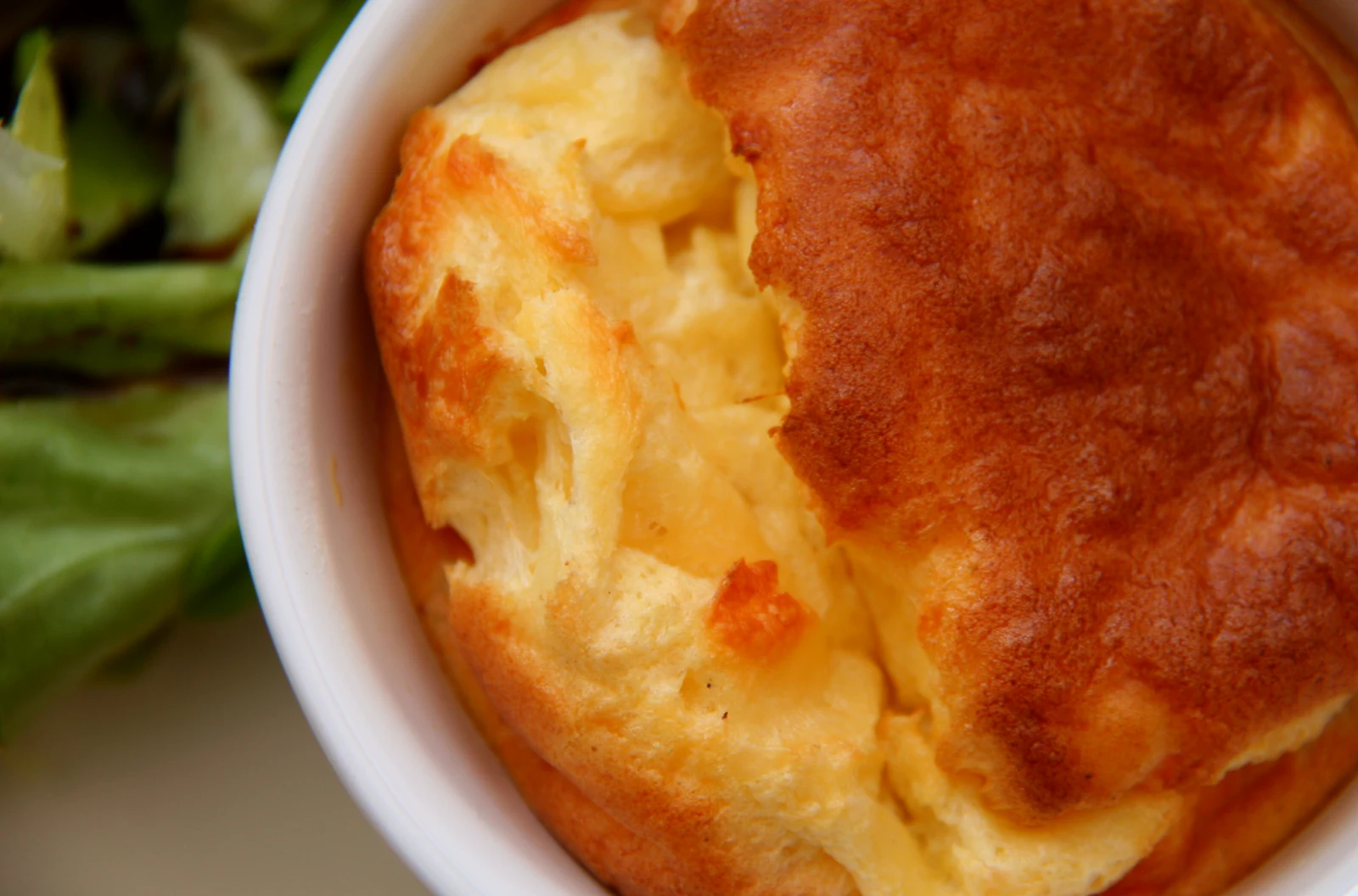 A golden French cheese souffle rising from a white ramekin